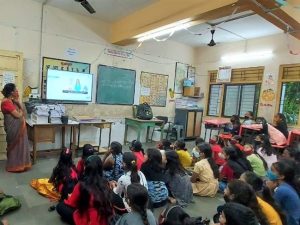 Ett klassrum av flickor i Indien där barnen sitter på golvet och kollar på nyheter.